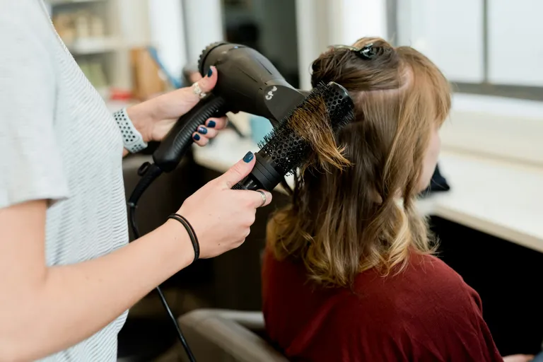 Cabeleireira finalizando o cabelo de uma cliente no salão