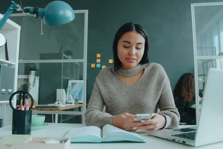 Mulher digitando no celular na mesa do escritório