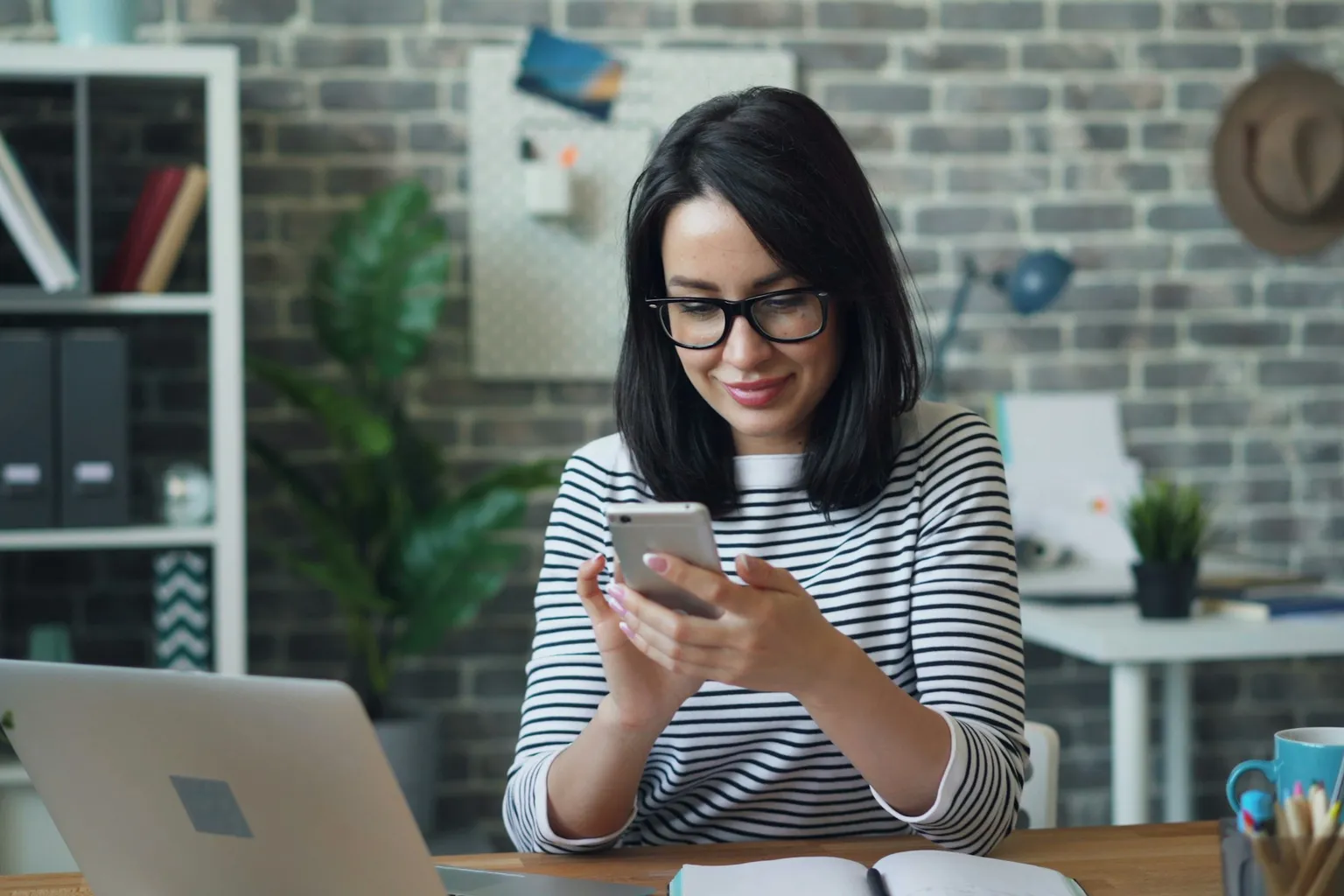 Mulher respondendo mensagens no celular, na mesa de trabalho
