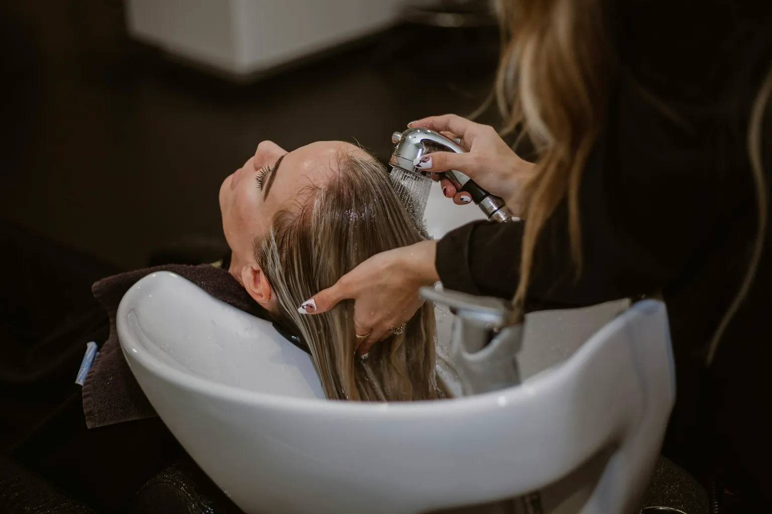 Cabeleireira lavando o cabelo de uma cliente no salão
